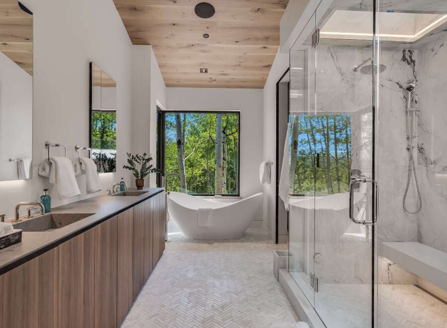 Experience luxury in this modern bathroom featuring a freestanding soaking tub with a stunning forest view.