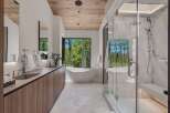 Experience luxury in this modern bathroom featuring a freestanding soaking tub with a stunning forest view.