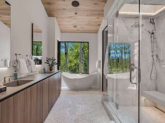 Experience luxury in this modern bathroom featuring a freestanding soaking tub with a stunning forest view.