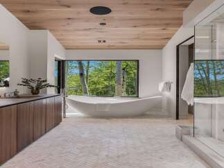 Experience luxury in this modern bathroom featuring a freestanding soaking tub with a stunning forest view.