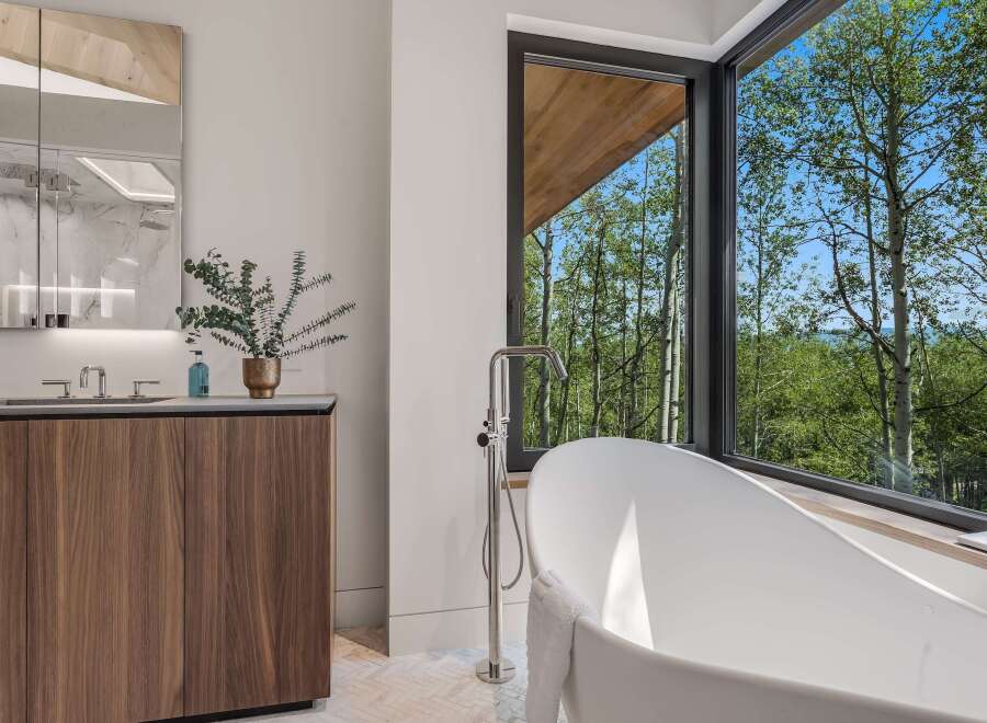 Experience luxury in this modern bathroom featuring a freestanding soaking tub with a stunning forest view.