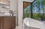 Experience luxury in this modern bathroom featuring a freestanding soaking tub with a stunning forest view.
