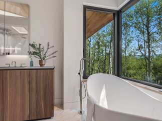 Experience luxury in this modern bathroom featuring a freestanding soaking tub with a stunning forest view.