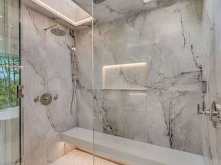 Experience ultimate relaxation in this luxurious marble shower, featuring a built-in bench and multiple shower heads for a spa-like experience.