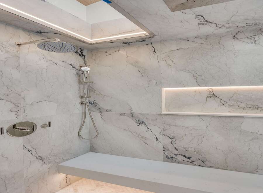 Experience luxury in this modern marble shower featuring a sleek rain showerhead and a built-in bench for ultimate comfort.