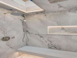 Experience luxury in this modern marble shower featuring a sleek rain showerhead and a built-in bench for ultimate comfort.