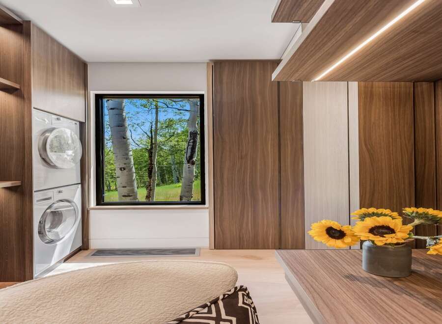 Experience modern living with this beautifully designed laundry space, featuring stacked white washers and dryers seamlessly integrated into rich walnut cabinetry.