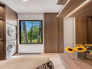 Experience modern living with this beautifully designed laundry space, featuring stacked white washers and dryers seamlessly integrated into rich walnut cabinetry.