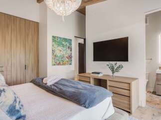 Experience modern luxury in this master bedroom featuring a king-sized bed with plush bedding and a striking abstract art piece.