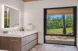 Experience modern luxury in this stunning bathroom, featuring a sleek vanity with integrated lighting and a large mirror reflecting the serene forest views.