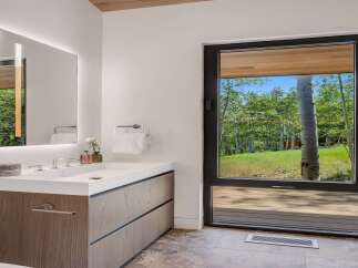 Experience modern luxury in this stunning bathroom, featuring a sleek vanity with integrated lighting and a large mirror reflecting the serene forest views.