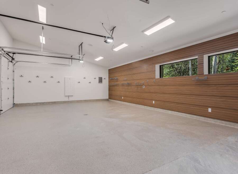 This spacious garage offers ample room for vehicles and storage, featuring a modern epoxy floor and a sleek wood-paneled accent wall.