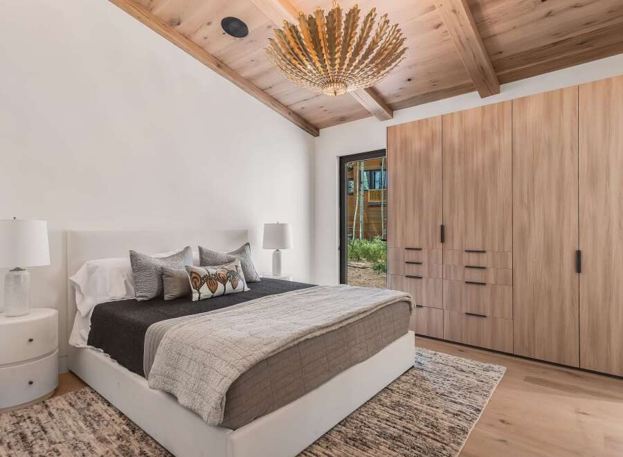 Experience luxury mountain living in this stunning bedroom featuring a vaulted wood-beamed ceiling and a striking modern chandelier.