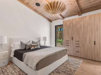 Experience luxury mountain living in this stunning bedroom featuring a vaulted wood-beamed ceiling and a striking modern chandelier.
