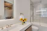 Experience modern luxury in this stunning bathroom featuring a sleek white vanity with contemporary chrome fixtures and a large, illuminated mirror reflecting a stylish bedroom.