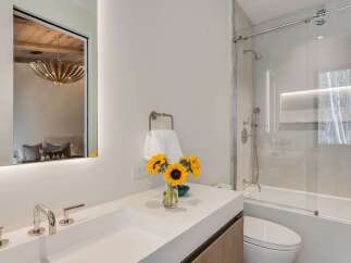 Experience modern luxury in this stunning bathroom featuring a sleek white vanity with contemporary chrome fixtures and a large, illuminated mirror reflecting a stylish bedroom.