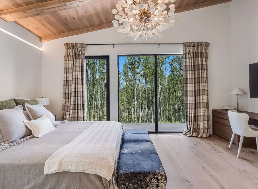Experience luxurious mountain living in this stunning bedroom featuring a vaulted wood-beamed ceiling and a dramatic chandelier.