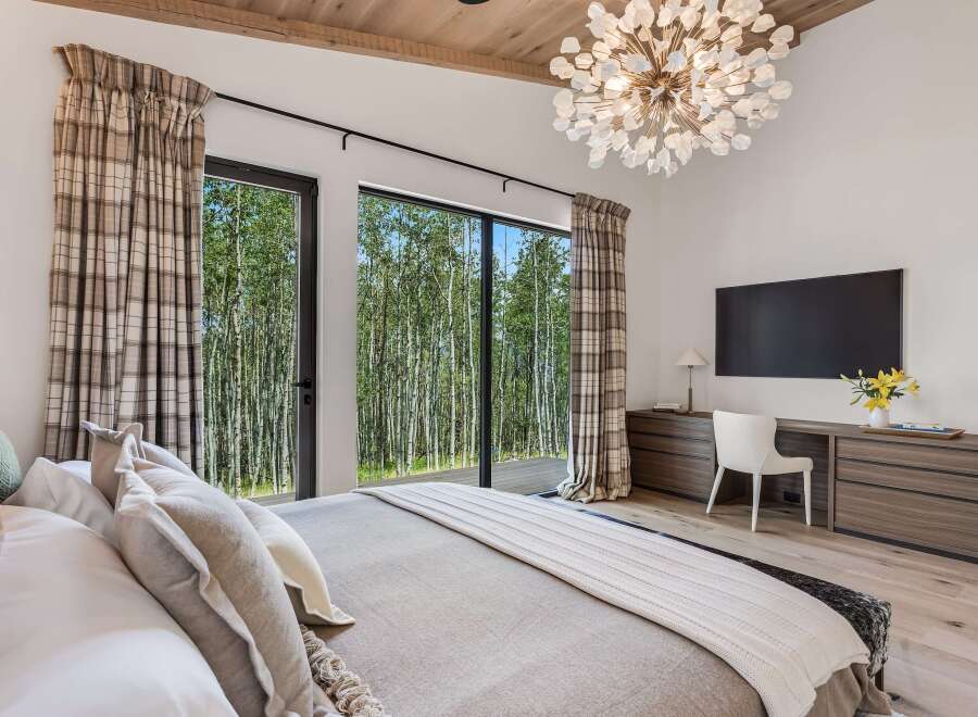 Experience luxury living in this stunning bedroom, featuring a dramatic vaulted ceiling with exposed wood beams and a statement chandelier.