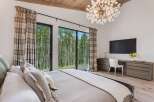 Experience luxury living in this stunning bedroom, featuring a dramatic vaulted ceiling with exposed wood beams and a statement chandelier.