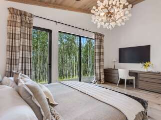 Experience luxury living in this stunning bedroom, featuring a dramatic vaulted ceiling with exposed wood beams and a statement chandelier.
