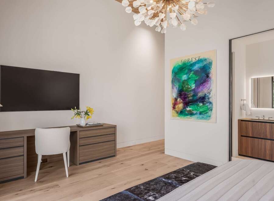 Experience modern luxury in this stunning bedroom featuring a sleek wall-mounted television and a stylish wooden desk with ample storage.