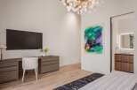 Experience modern luxury in this stunning bedroom featuring a sleek wall-mounted television and a stylish wooden desk with ample storage.