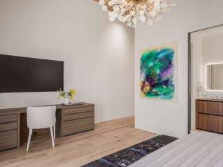 Experience modern luxury in this stunning bedroom featuring a sleek wall-mounted television and a stylish wooden desk with ample storage.