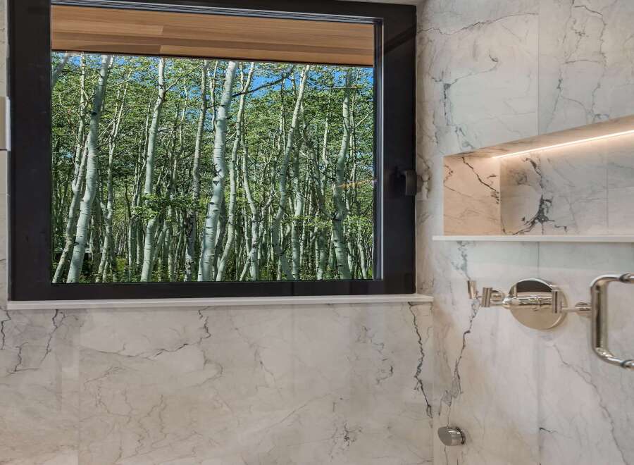 Experience the tranquility of nature from this stunning bathroom, featuring a large window that frames a breathtaking view of a lush forest.