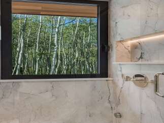 Experience the tranquility of nature from this stunning bathroom, featuring a large window that frames a breathtaking view of a lush forest.