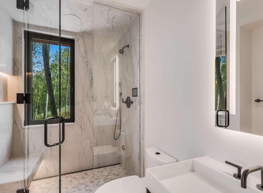 Experience luxury in this modern bathroom featuring a spacious walk-in shower with marble tile and a built-in bench.