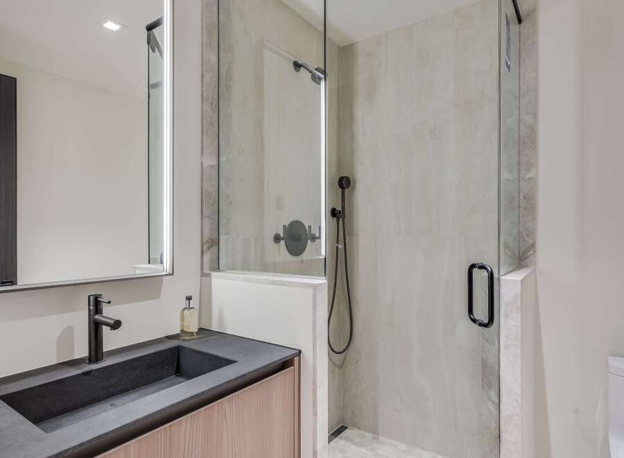 Experience modern luxury in this bathroom featuring a sleek vanity with a dark stone countertop and a minimalist black faucet.