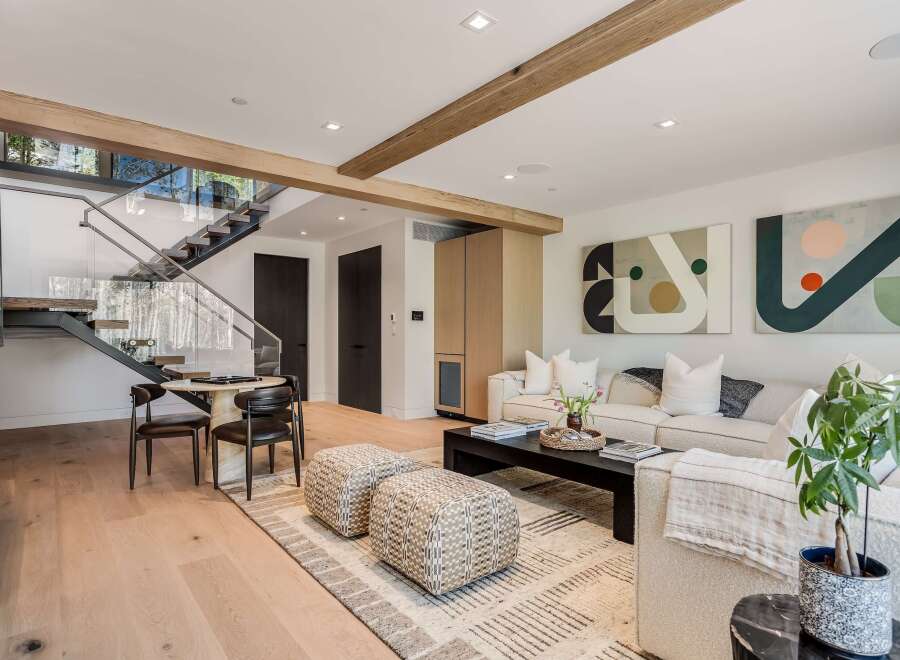 Experience modern living in this stunning open-concept space, featuring a sleek floating staircase with glass railings and exposed wooden beams.