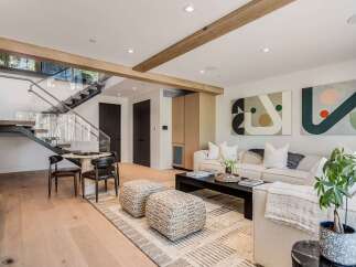 Experience modern living in this stunning open-concept space, featuring a sleek floating staircase with glass railings and exposed wooden beams.