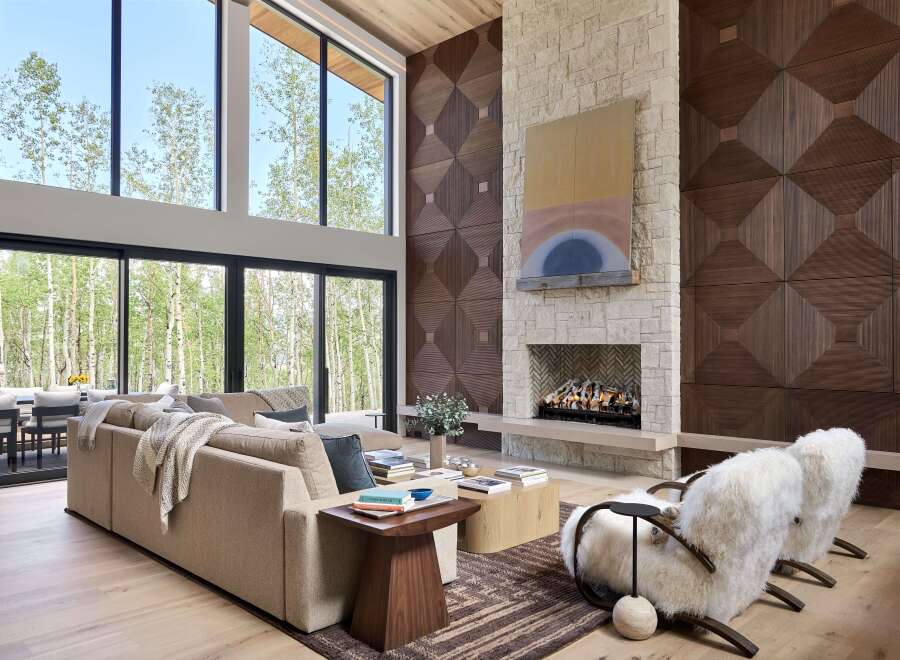 Experience luxury living in this stunning modern great room, featuring soaring ceilings and expansive windows that offer breathtaking views of the surrounding forest.