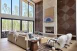 Experience luxury living in this stunning modern great room, featuring soaring ceilings and expansive windows that offer breathtaking views of the surrounding forest.