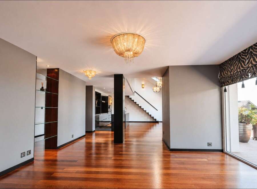 Experience modern luxury in this spacious open-plan living area, featuring gleaming hardwood floors and elegant ceiling light fixtures.
