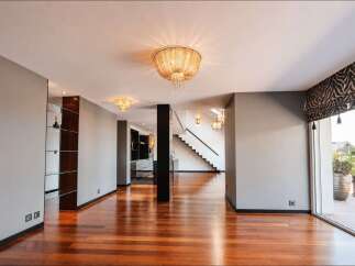 Experience modern luxury in this spacious open-plan living area, featuring gleaming hardwood floors and elegant ceiling light fixtures.