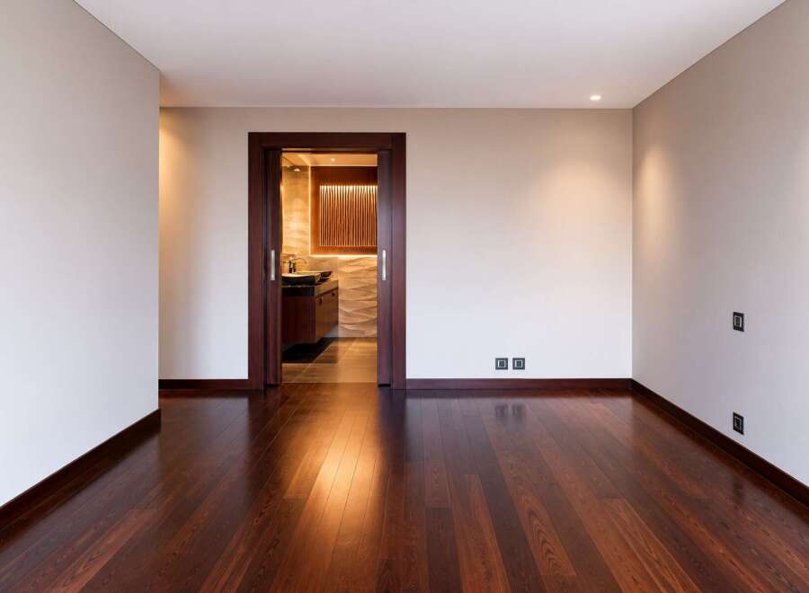 Experience modern luxury in this spacious room featuring a rich, dark hardwood floor that gleams under recessed lighting.