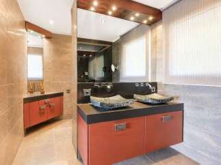This modern bathroom features a double vanity with unique stone vessel sinks and sleek orange cabinetry.