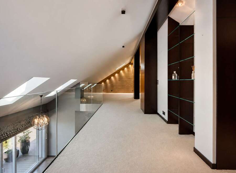 Experience modern luxury in this spacious loft-style hallway, featuring a sleek glass railing overlooking a balcony with lush greenery.