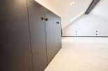 Discover this modern attic space featuring a sleek, dark wood built-in wardrobe with unique decorative handles.