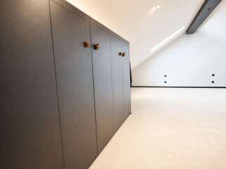 Discover this modern attic space featuring a sleek, dark wood built-in wardrobe with unique decorative handles.