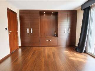 Experience modern living in this spacious room featuring a stunning floor-to-ceiling wooden wardrobe with integrated shelving and subtle lighting.