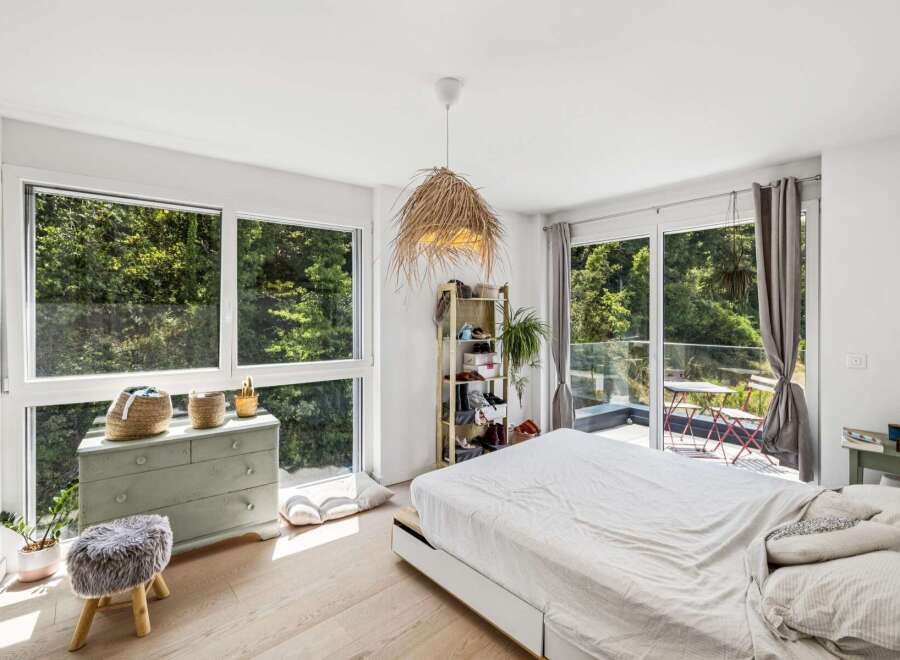 Experience serene living in this bright bedroom, featuring expansive windows that offer breathtaking views of lush greenery.