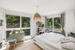 Experience serene living in this bright bedroom, featuring expansive windows that offer breathtaking views of lush greenery.