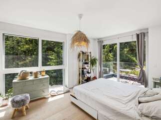 Experience serene living in this bright bedroom, featuring expansive windows that offer breathtaking views of lush greenery.