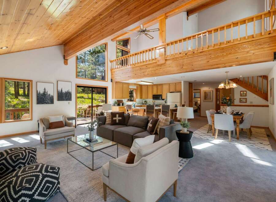 Experience rustic charm and modern comfort in this spacious living area, featuring a soaring wood-beamed ceiling and abundant natural light pouring in through large windows.