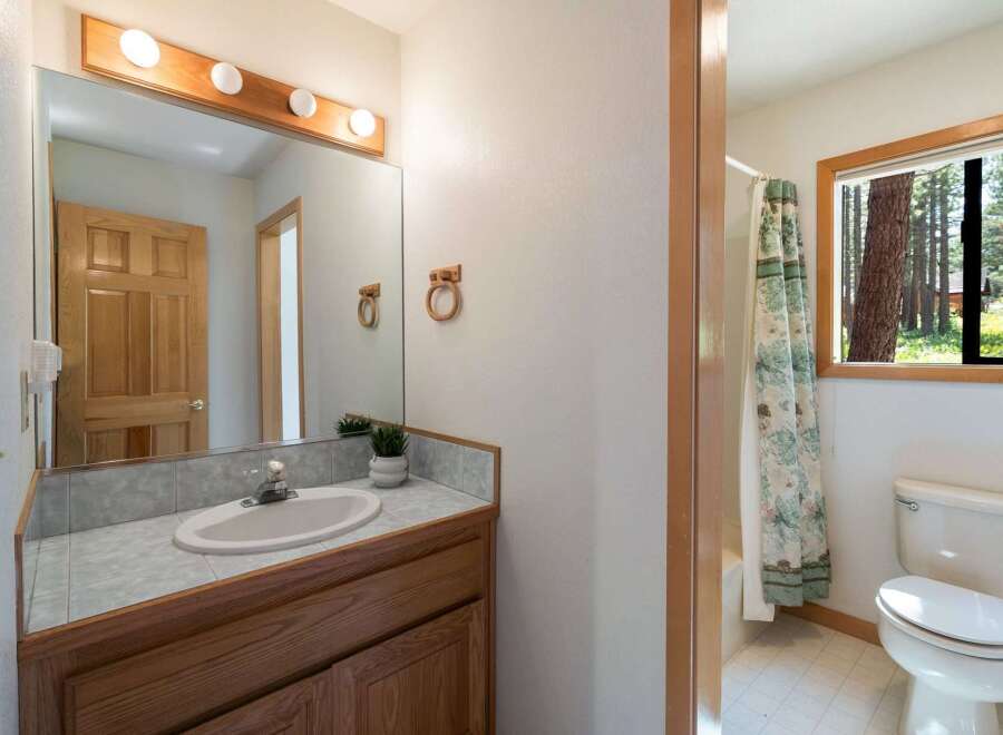 This charming bathroom features a wooden vanity with a tiled countertop and a white sink, complemented by a large mirror with a wooden frame and vanity lights.