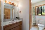 This charming bathroom features a wooden vanity with a tiled countertop and a white sink, complemented by a large mirror with a wooden frame and vanity lights.