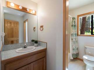 This charming bathroom features a wooden vanity with a tiled countertop and a white sink, complemented by a large mirror with a wooden frame and vanity lights.